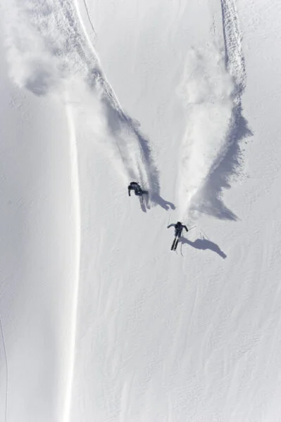 Aerial view of two skiers skiing downhill in powder snow