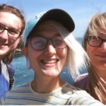 Summer Taylor smiling while outdoors with their brother Luke, and mother Dalia, wearing glasses, a light blue baseball cap, and a striped shirt, with sunlight on their face. Taylor was a peaceful Black Lives Matter protester tragically killed during a July 2020 protest in Seattle.