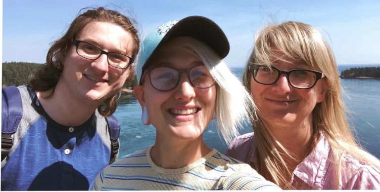 Summer Taylor smiling while outdoors with their brother Luke, and mother Dalia, wearing glasses, a light blue baseball cap, and a striped shirt, with sunlight on their face. Taylor was a peaceful Black Lives Matter protester tragically killed during a July 2020 protest in Seattle.